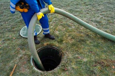 a man in blue overalls holding a hose into a hole in the grass